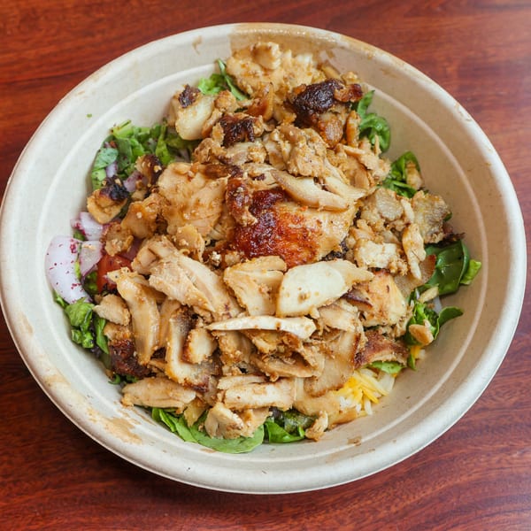 A close-up of a chicken shawarma bowl with rice, lettuce, and red onions in a paper bowl.