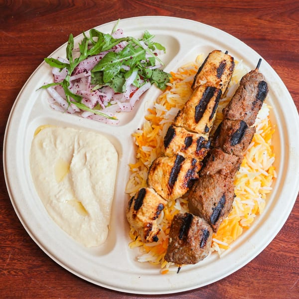 Grilled chicken and beef skewers with rice, hummus, and a side salad on a divided plate.