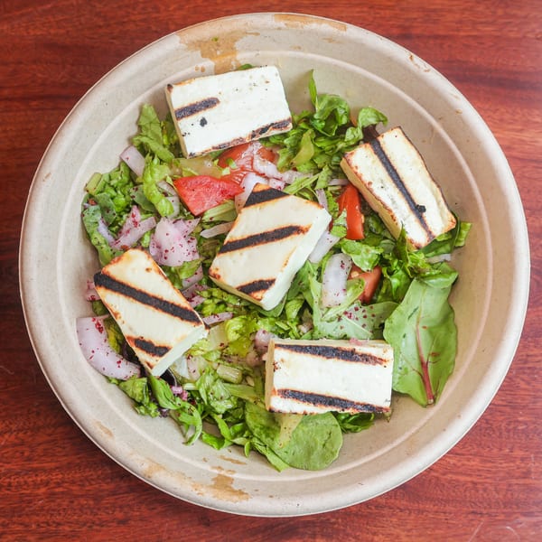 Overhead view of a salad with grilled halloumi cheese, lettuce, tomatoes, and red onions.