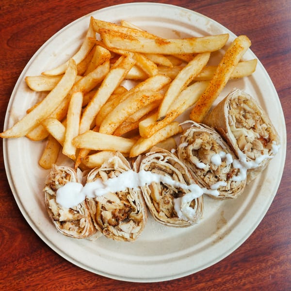 Chicken shawarma wraps with white sauce and a side of seasoned french fries on a plate.