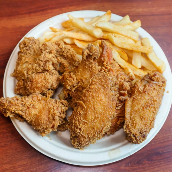 A white plate filled with golden-brown fried chicken pieces and a side of french fries.