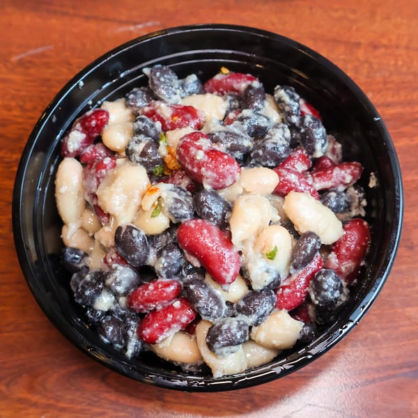 A black bowl filled with a bean salad featuring white, red, and black beans in a creamy dressing.