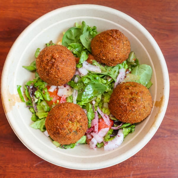 Four crispy falafel balls atop a fresh green salad with red onions and tomatoes in a bowl.