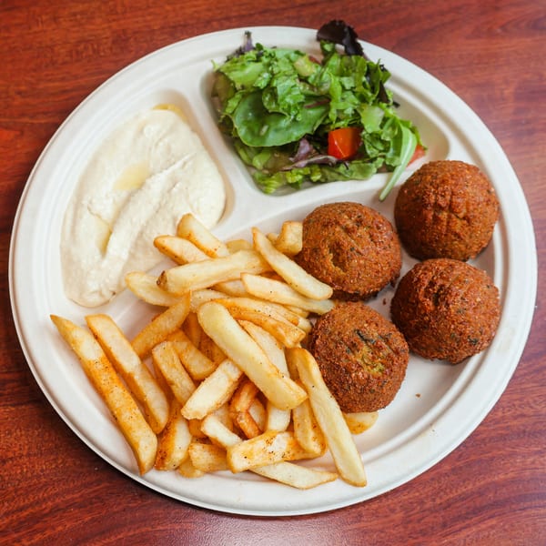 A divided plate with falafel, french fries, hummus, and a side salad on a wooden table.
