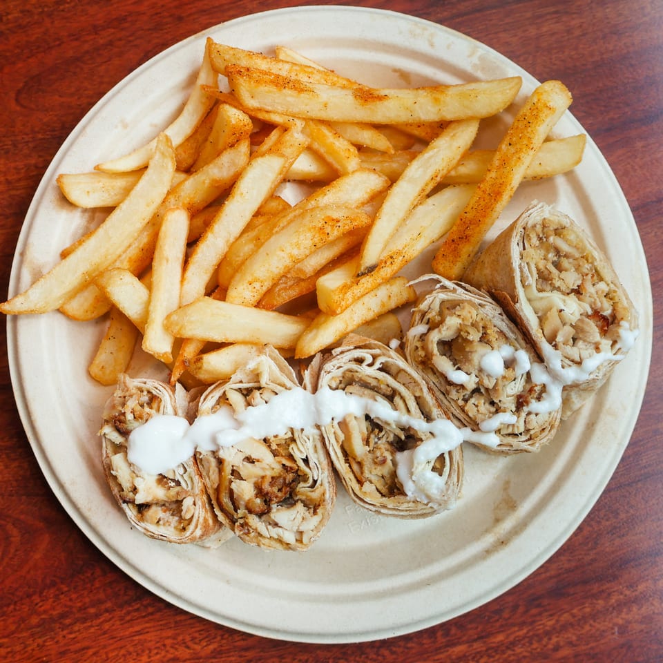 Chicken shawarma wraps with white sauce and a side of seasoned french fries on a plate.